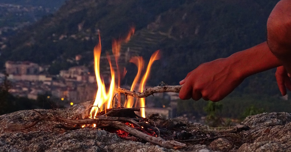 Picture of a campfire, fire with a hand holding a stick over the campfire.