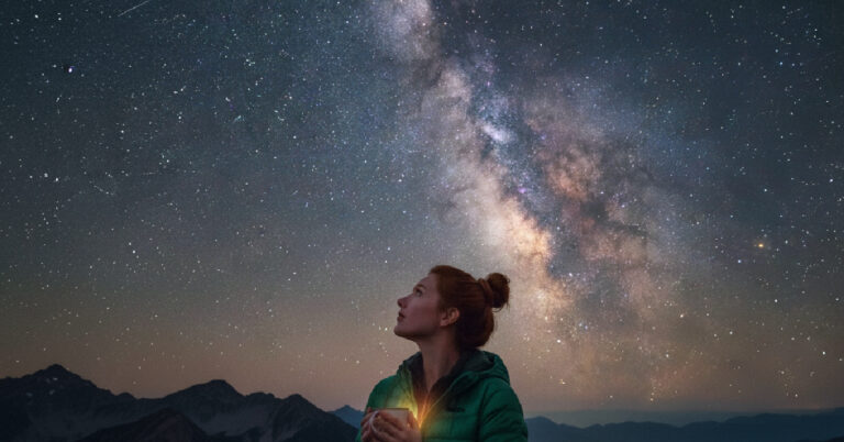 A woman looking up at milky way holding a mug.