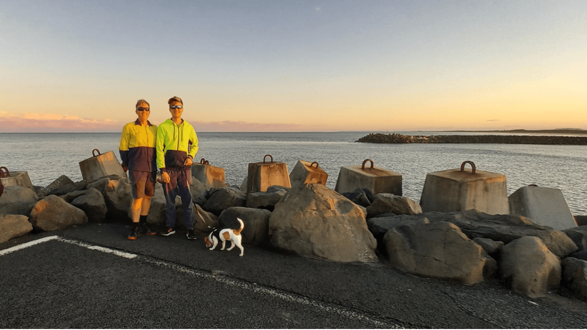 Brad and Toby Woolcott on Ballina North Wall 2023, river in the background. Jack Russel on a lead.
