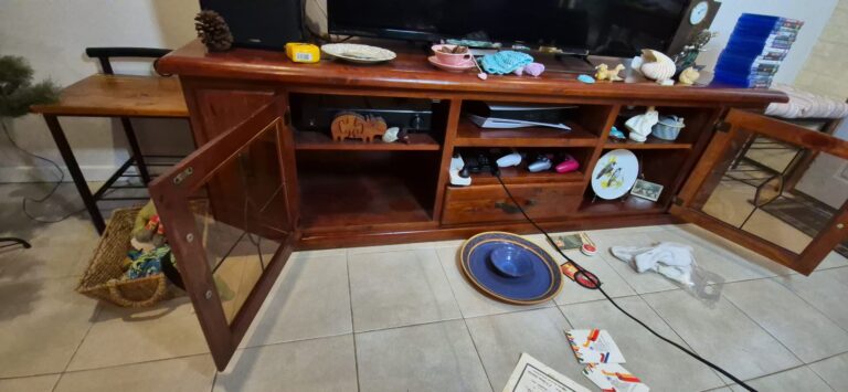 Wooden television cabinet with two glass doors, mess of organising dishes, ornaments and keepsakes.