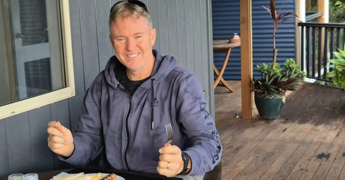 bed and breakfast misty morning wordpress Brad smiling at the camera while sitting at a table on a wooden verandah, holding a knife and fork to eat a cooked breakfast.